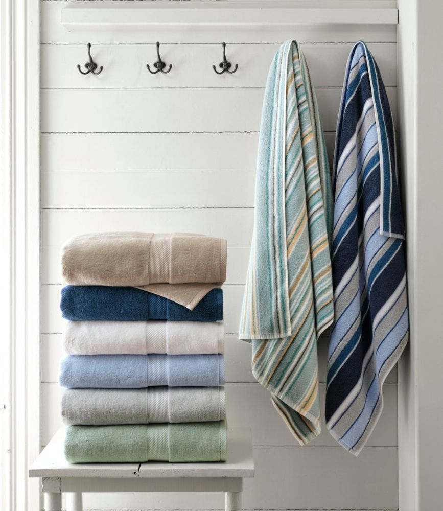 Stacked solid-color cotton towels and two striped bath towels hanging on hooks in a white bathroom.