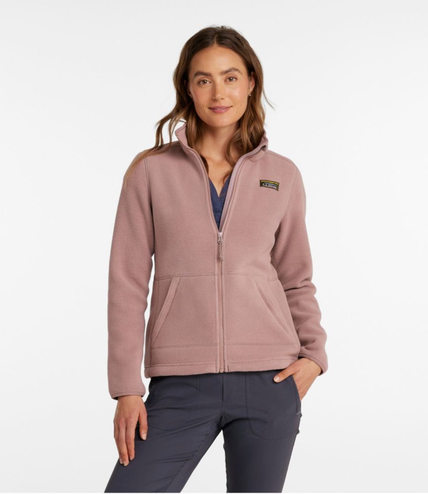 Women’s mauve zip-front fleece jacket with stand collar and front pockets, worn over a V-neck top and hiking pants.