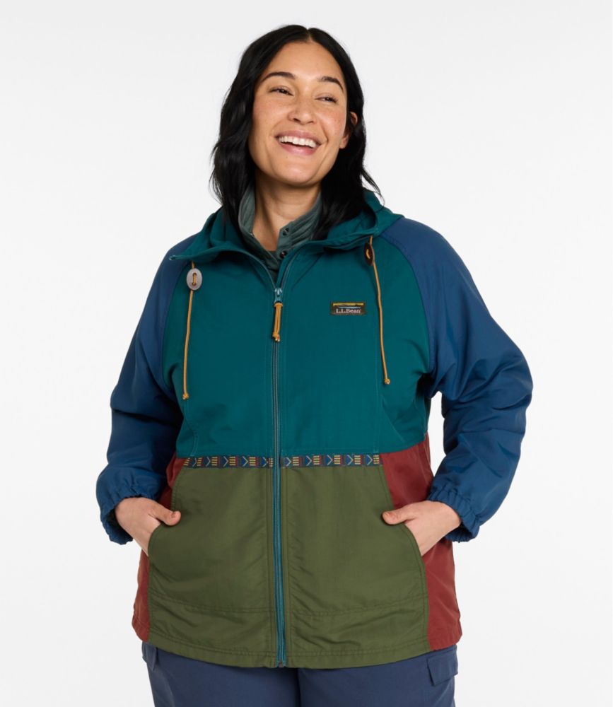 Woman wearing a multi-color full-zip hooded jacket with teal, blue, olive, and rust panels and front pockets.
