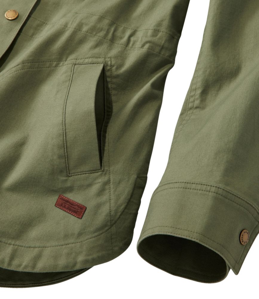 Women’s olive green utility jacket close-up showing front pocket, curved hem, and cuff with snap detail.