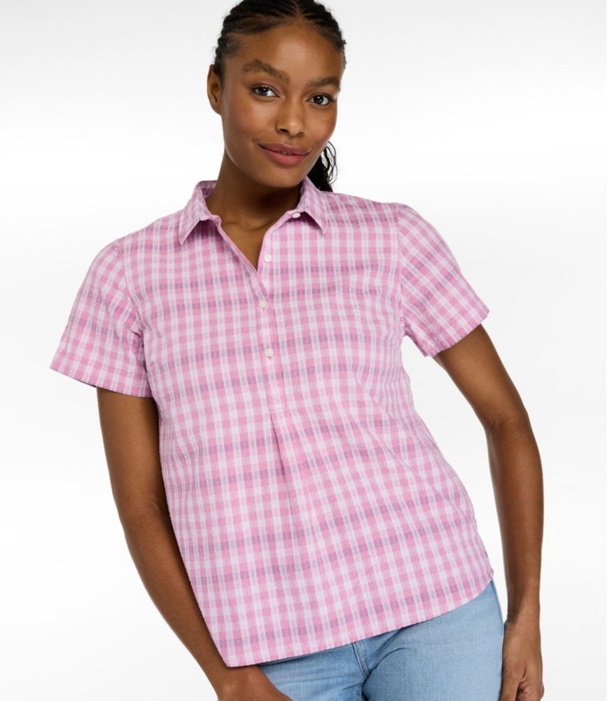 Woman wearing a pink and white gingham short-sleeve seersucker popover shirt with collar and buttons, paired with light jeans.