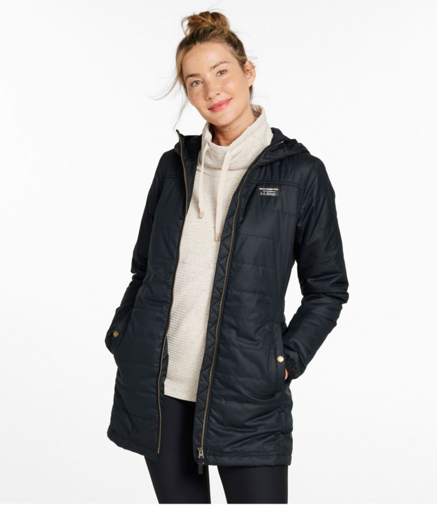 Woman wearing a thigh-length navy puffer coat with hood, front zipper and snap pockets over a light hoodie.