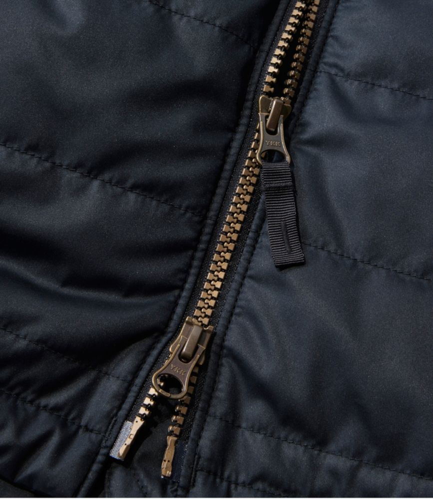Close-up of women’s navy puffer coat showing dual metal front zippers with fabric pull tab.