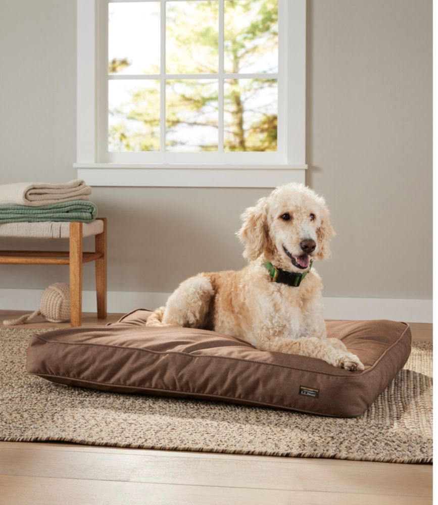 Medium rectangular burlap-colored denim dog bed with a dog lounging on it in a living room by a window.