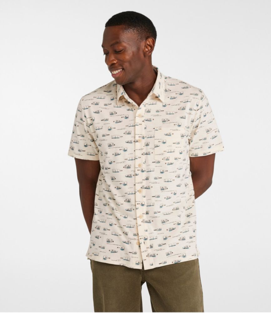 Men's beige short-sleeve button-front shirt with small blue and gray camper print, worn untucked by a standing model.