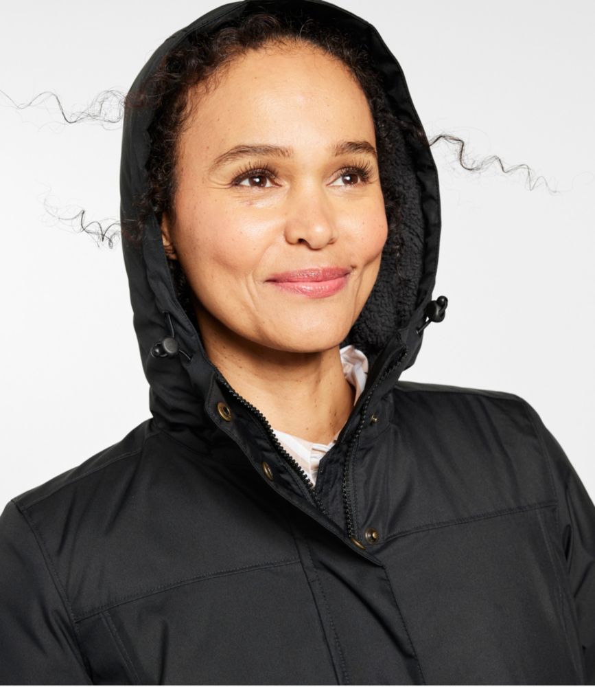 Woman wearing a black winter coat with fleece-lined hood and high zip front, shown from the chest up.