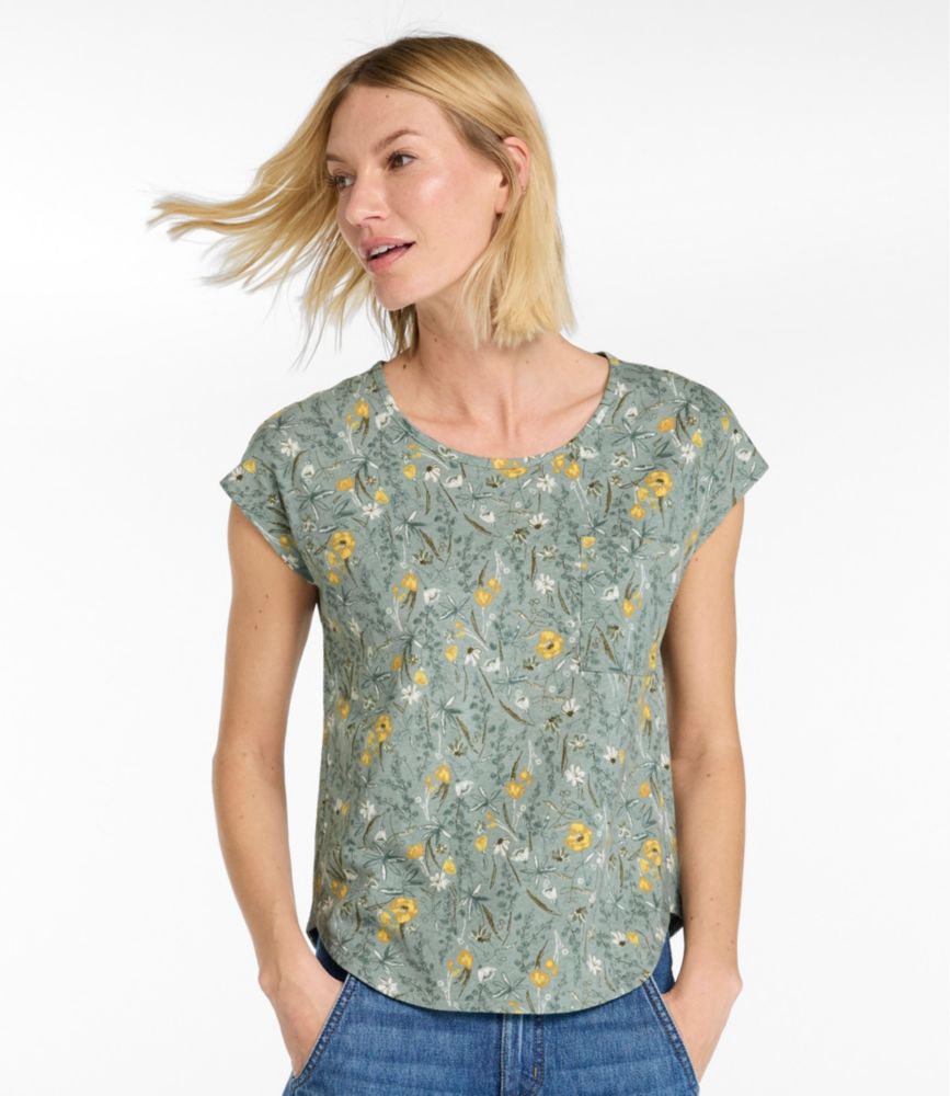 Women’s sage green linen-cotton scoopneck tee with yellow floral print, shown front-facing on model with hands in jeans pockets.