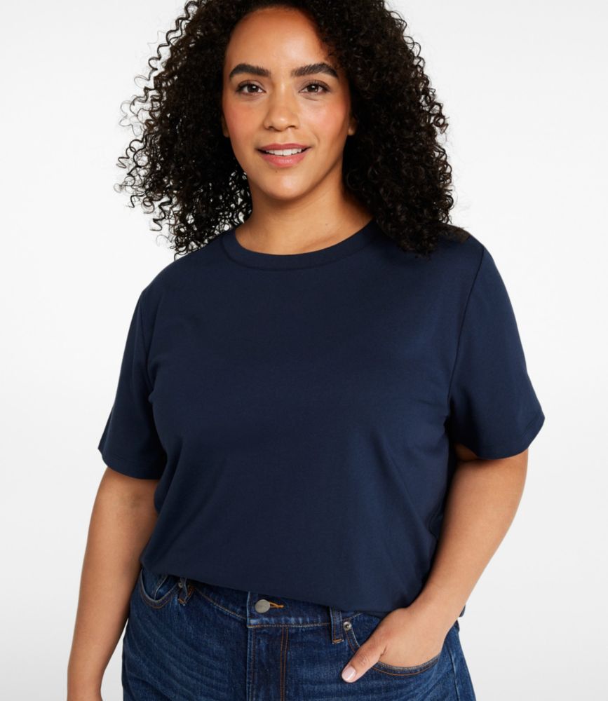 Woman wearing a navy short-sleeve crewneck cotton tee tucked into dark blue jeans.