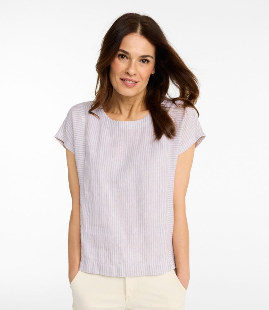 Women’s short-sleeve striped linen boatneck shirt in light sand and white, shown on model front view with hands in pockets.
