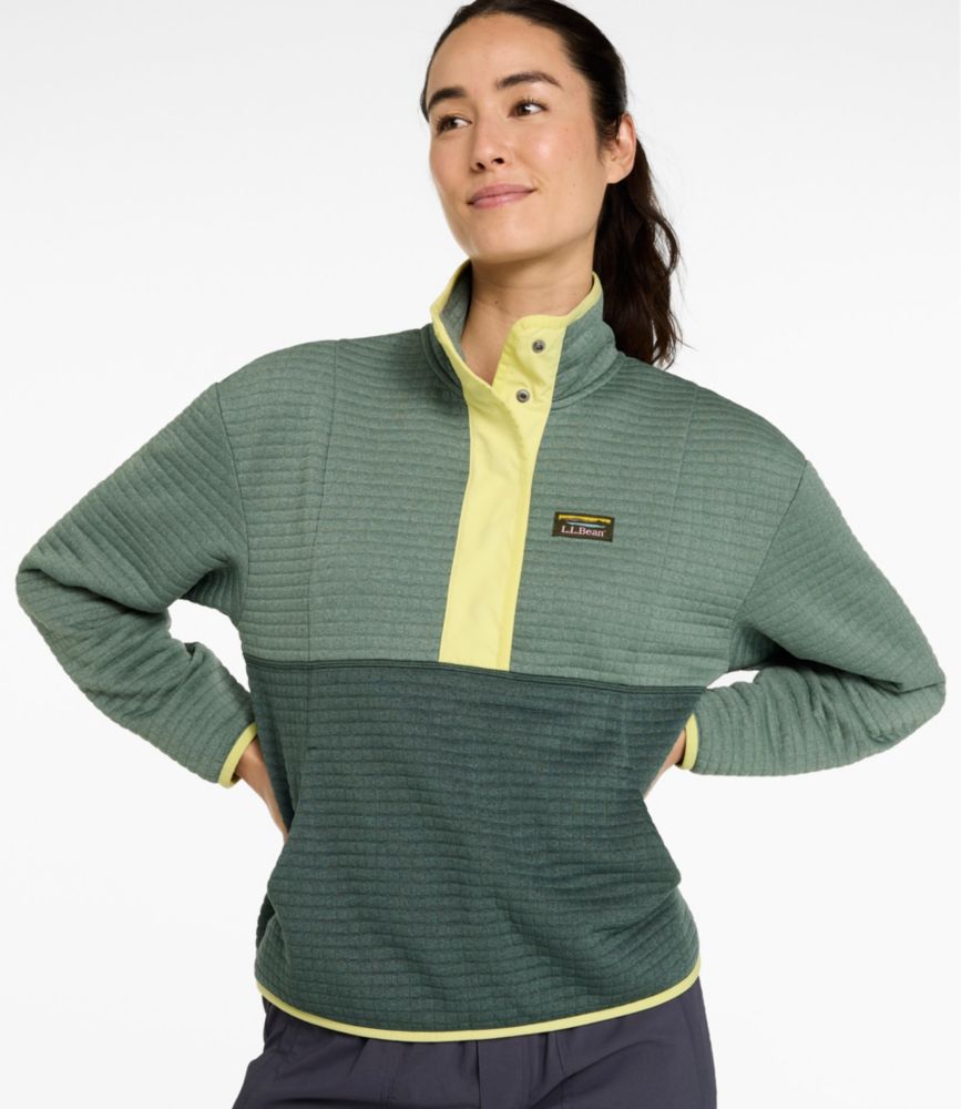 Woman wearing a green colorblock grid fleece pullover with yellow snap neck placket and logo patch, hands on hips.