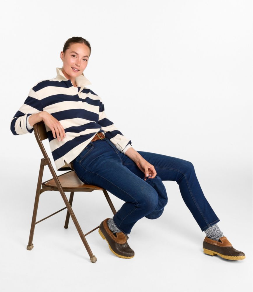 Woman seated in a chair wearing a navy and cream striped long-sleeve rugby shirt with jeans and duck shoes.